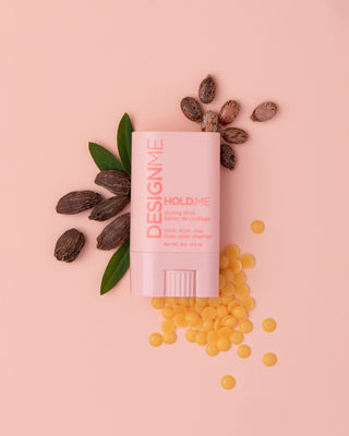 DESIGNME HOLD.ME Styling Stick product front view surrounded by key ingredients like jojoba, castor seeds and candellila wax