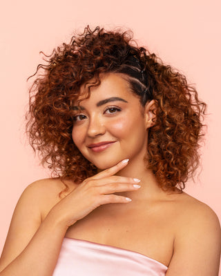 Model applies DESIGNME HOLD.ME Three-Way Hairspray for sleek style on one side of her curly hair.