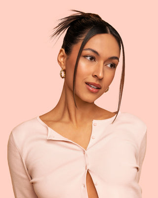 A model wears a sleek bun with styled front hair, showcasing a glossy, polished finish after using the HOLD.ME styling duo.